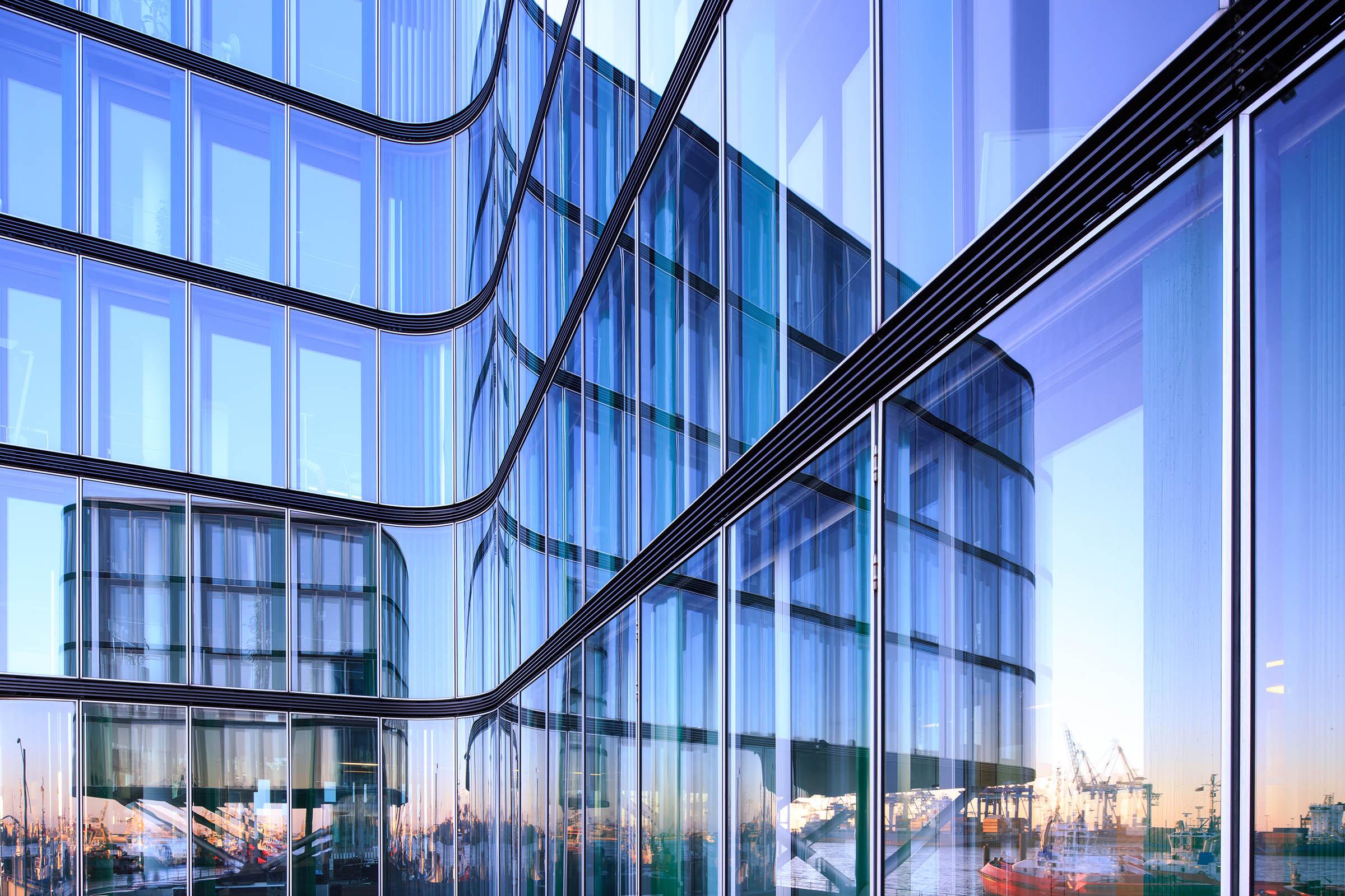 Bläulich schimmernde Glasfront eines Gebäudes mit Spiegelung anderer Gebäude