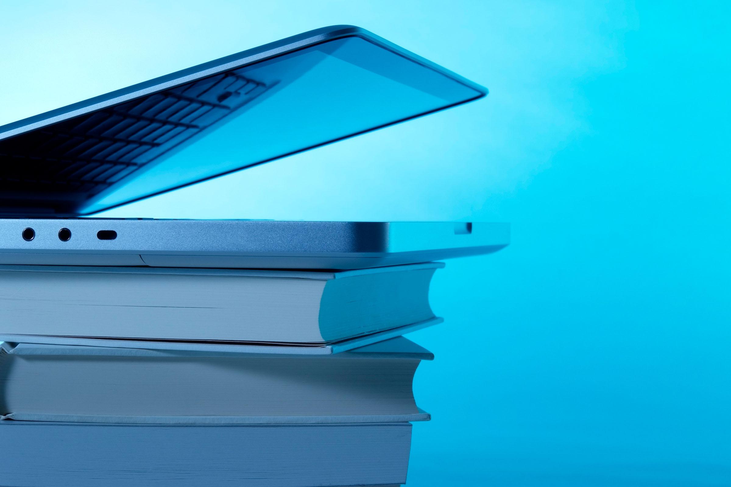 Auf einem Stapel Bücher liegt ein halb geöffneter Laptop