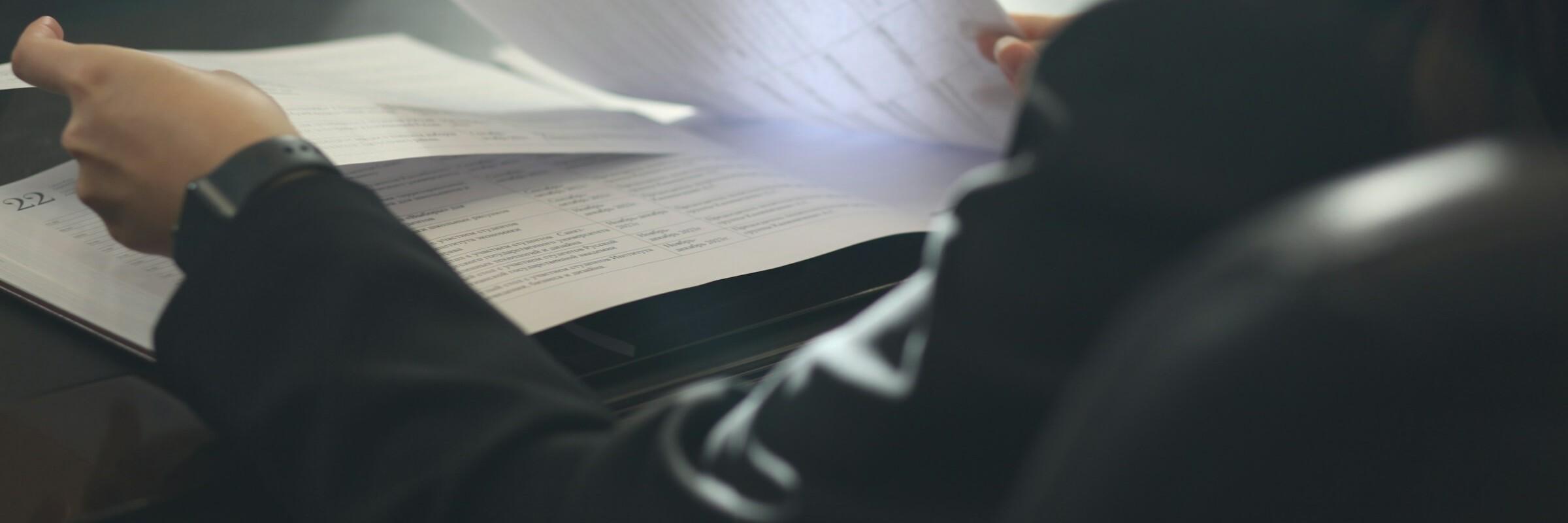 Vertrag Man sieht einer Person über die Schulter, die mit ihren Händen gerade Dokumente durchblättert