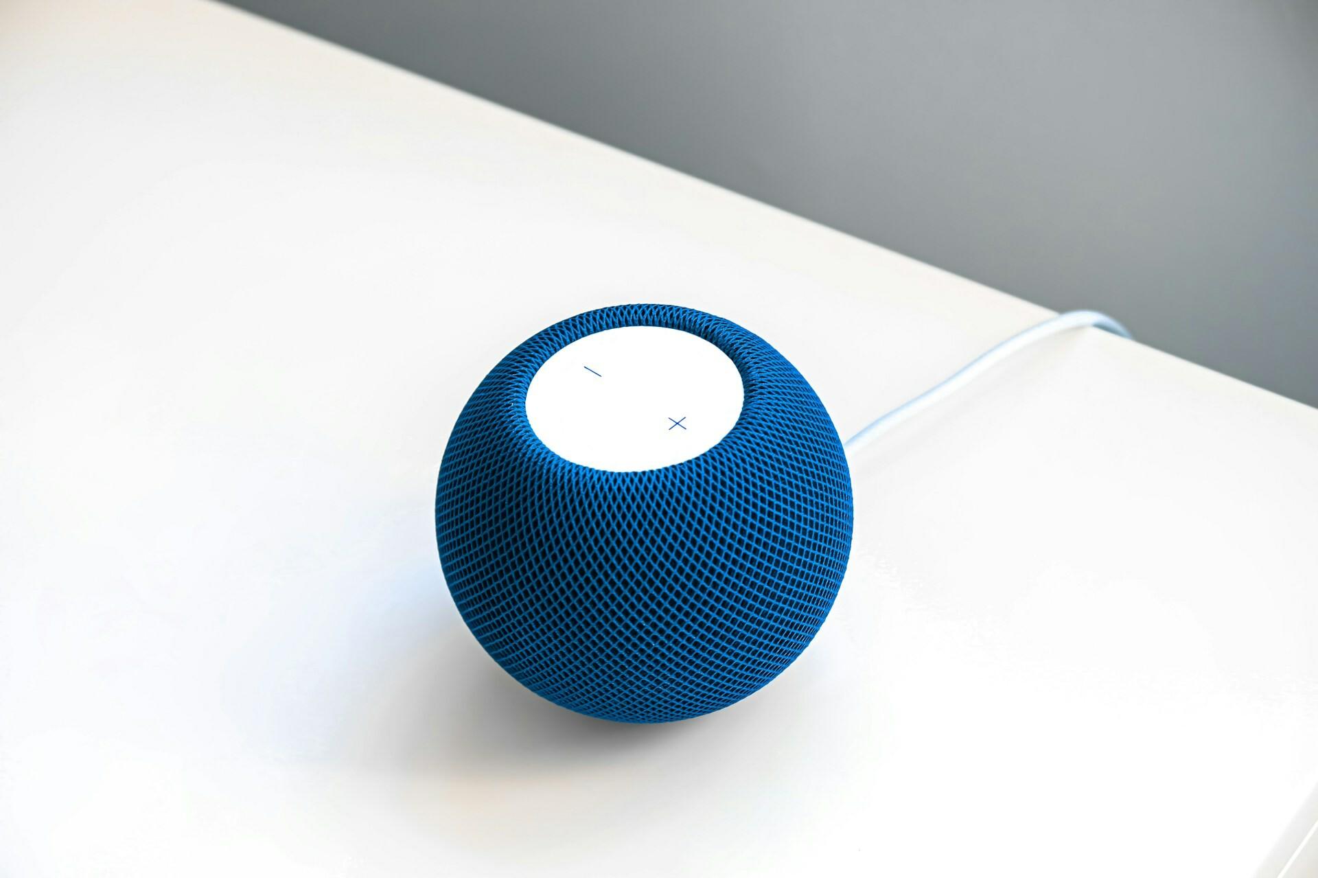 Intelligenter blauer Lautsprecher A smart blue speaker lies on a white table.