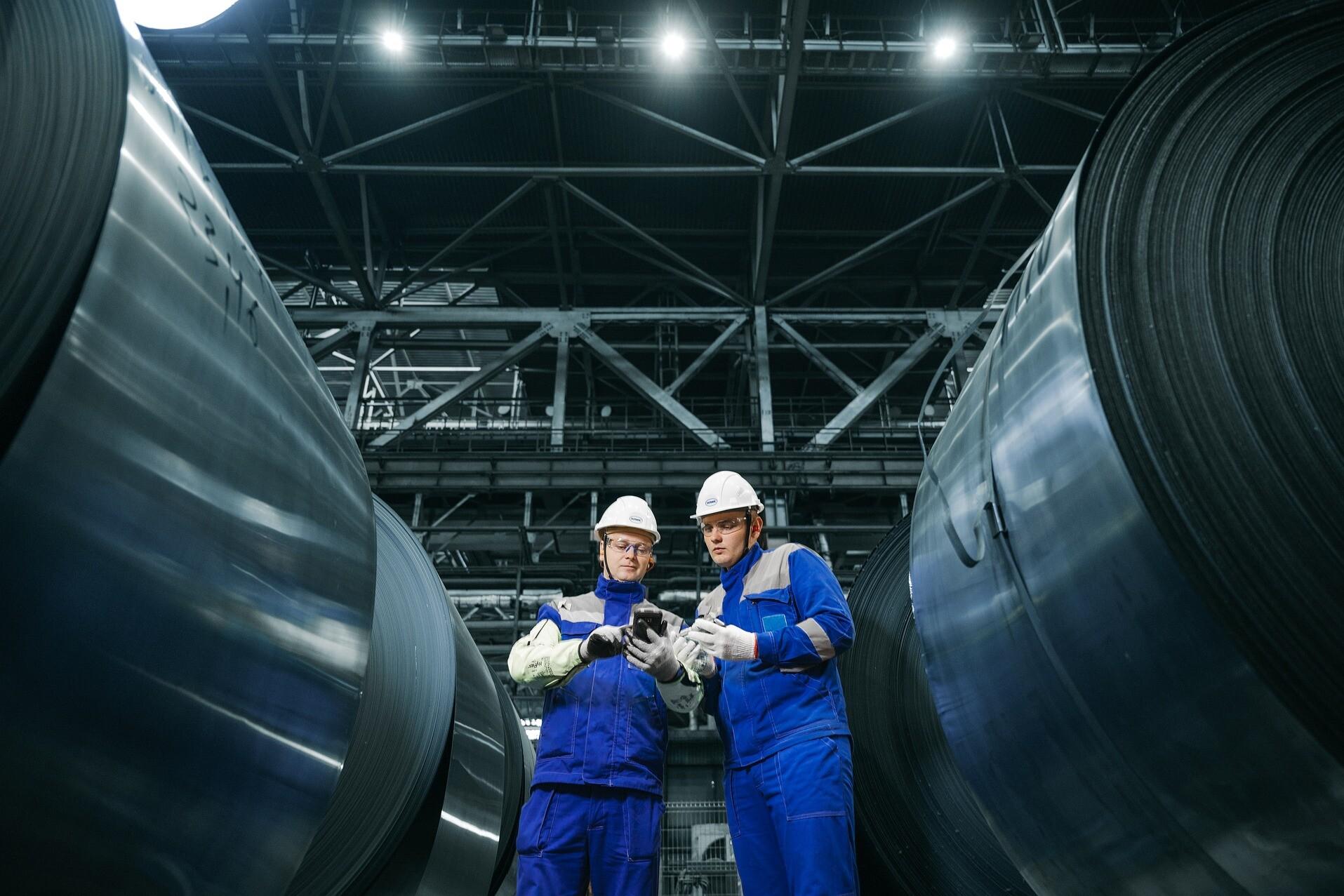 Zwei Personen in einer Maschinenhalle Two people wearing protective helmets are standing between two machines and checking something.
