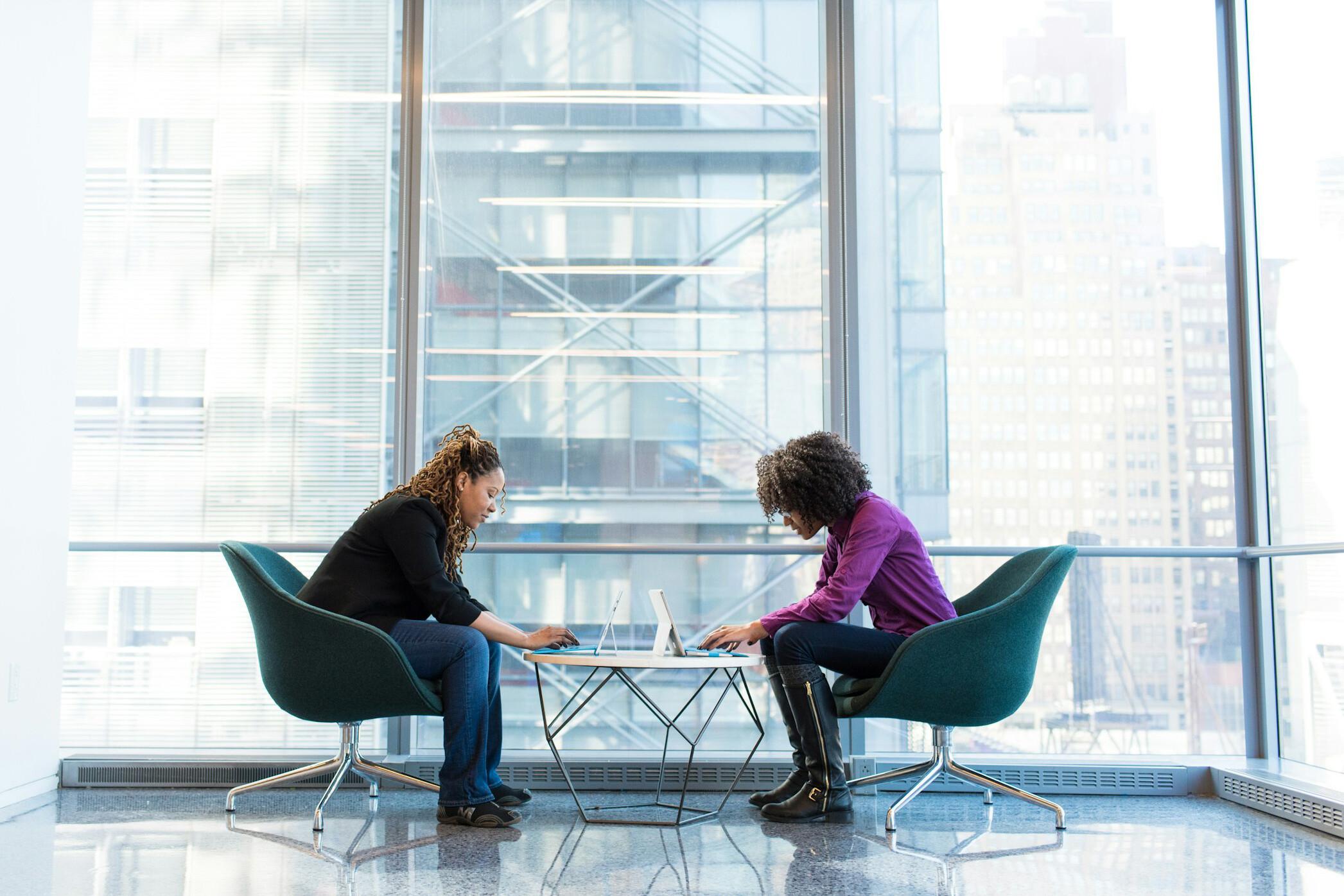 Gespräch Zwei Frau sitzen in einem Glasgebäude gegenüber an einem Tisch