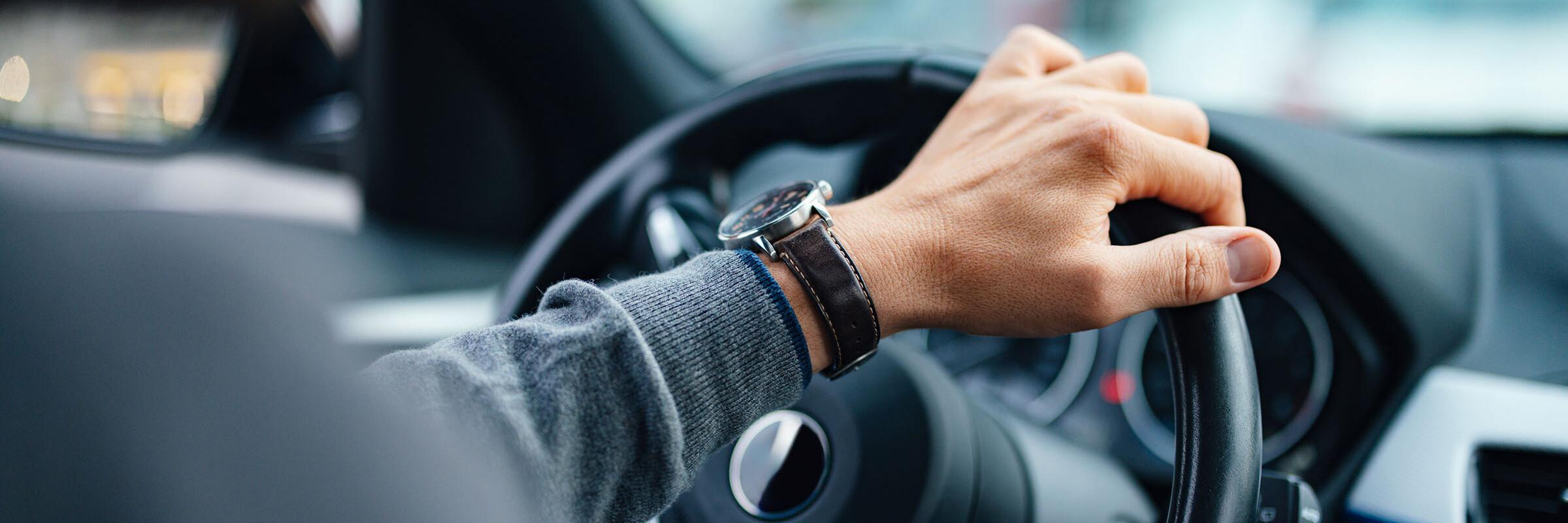 Hand am Lenkgrad Eine Hand mit Uhr lenkt das Lenkrad eines Autos