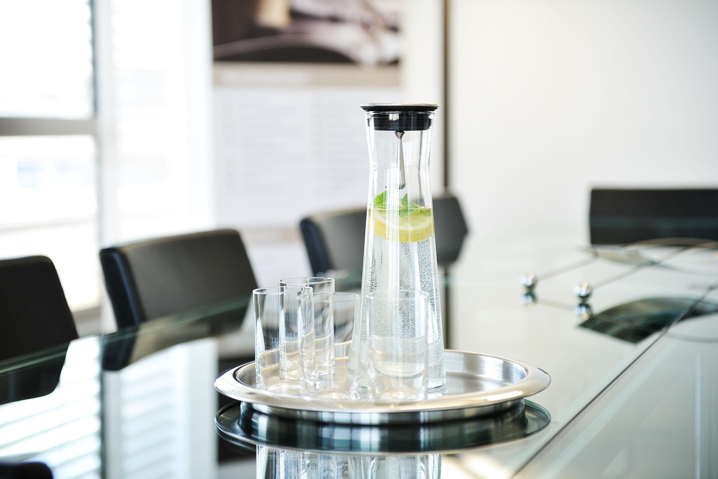 Glaskaraffe auf Glastisch Glaskaraffe mit Wasser und einer Zitrone darin steht mit einigen Gläsern auf einem Tablett auf einem Glastisch in einem Konferenzraum