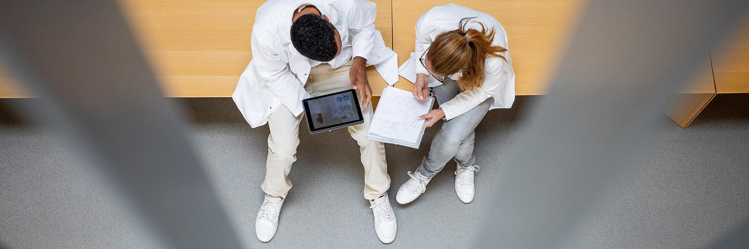 Zwei Ärzte im Gespräch Zwei Ärzte sitzen auf einer Bank und tauschen sich über Dokumente aus